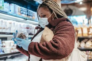 Image of a person wearing gloves and a face mask, carefully reading a food product label at the supermarket