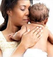 A baby being burped over the shoulder of a parent, with the parent gently patting their back