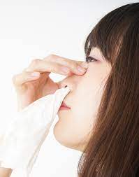 Woman blowing her nose in a tissue, potential sign of high blood pressure complications.