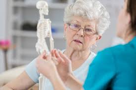 Healthcare professional holding small skeleton while explaining elderly care to elderly woman