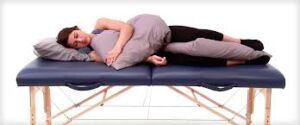 A person lying on their side with a pillow tucked between their legs for hip and spine alignment. Another pillow is placed under their head and arms for added support and comfort.