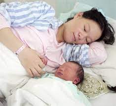 Woman sleeping in bed next to her baby: traditional postpartum practices