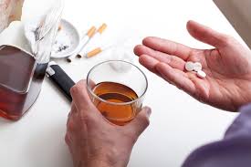 Individual holding alcohol and medication - illustrating the risks of mixing substances. Cigarettes on table emphasize potential health hazards.
