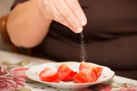 Image of a person sprinkling salt on a fresh tomato salad as part of dietary habits.