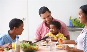 Happy family seated at the table, enjoying a nutritious meal together, emphasizing the importance of not skipping meals and eating on time for a healthy lifestyle.