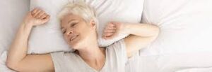 Image of a woman in bed, stretching and feeling rejuvenated after enjoying a night of quality rest. Achieve optimal well-being with good sleep habits.