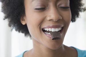 Smiling woman enjoying dark chocolate, a common myth associated with acne