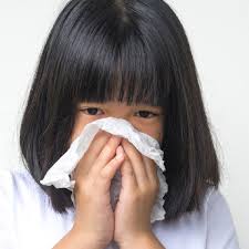 Image of a girl blowing her nose into a tissue, experiencing allergies symptoms.