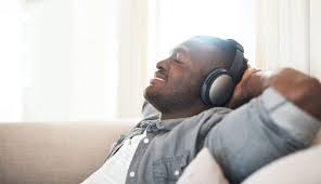 Man relaxing on the couch, listening to music, and smiling. Experience a moment of joy and mental refreshment through music and relaxation.