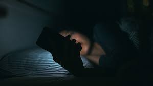 Person in bed using phone in the dark due to insomnia