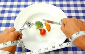 Person with hands tied with tape measure to plate with vegetables, holding spoon and fork: Fad diets and portion control.