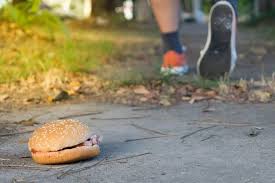 A discarded burger on the ground with a person in training sneakers: Choosing healthy over unhealthy foods