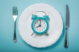 Clock set at dinner table with empty plate - Illustration depicting the concept of intermittent fasting, with a clock placed on a dinner table next to an empty plate.