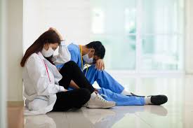 Two healthcare workers facing mental health challenges, sitting on floor and resting against the wall