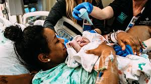 Newly delivered woman holding her baby while healthcare professional tends to the baby - A significant moment captured as a mother embraces her newborn while a healthcare professional tends to the baby, reflecting elements of the birth plan in action.