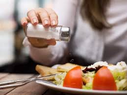 Person adding salt to salad - An image showing a person sprinkling salt over a plate of salad, illustrating the potential addition of excessive sodium to otherwise healthy food.