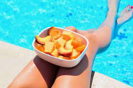Poolside serenity: person enjoying fruits with feet in the water