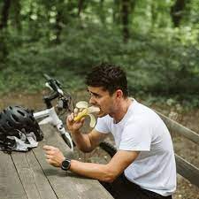 Man eating a banana on a park bench, emphasizing nutrition during a cycling break.