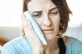 Woman in pain with cold compress on cheek - demonstrating cold compress remedy for toothache relief.