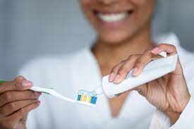 Woman smiling as she applies toothpaste to a toothbrush, emphasizing dental health routine.