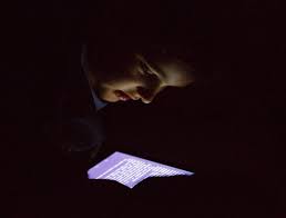 Person engrossed in reading on a mobile device in a dimly lit room, emphasizing vision concerns