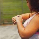 Person taking a break from exercise, checking their watch, emphasizing the importance of pacing in weight loss routines.