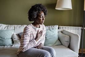 Woman seated on a chair, visibly distressed and clutching her chest due to heartburn discomfort.