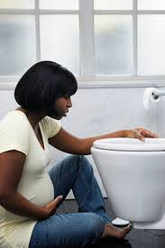 pregnant woman experiencing morning sickness seated in front of a toilet